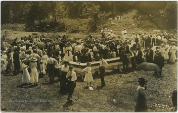 A crowd gathered in the center of the photograph eats, dines, and converses with associates. 