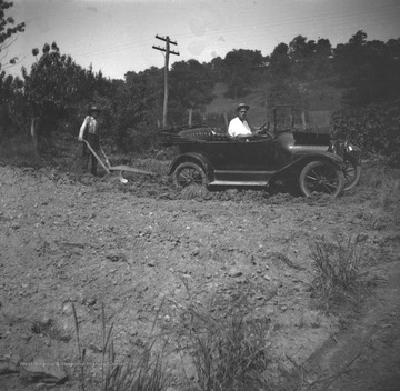 Two men, likely members of the Green family, are operating a plow attached to an automobile.  One man drives the car and the other guides the plow.