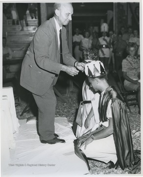 The health king and queen kneel before an altar as they get crowned. 