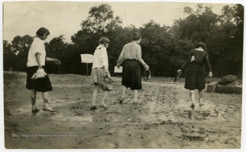 Four barefoot women walk through mud towards the Lewis County Cottage at a 4-H camp.