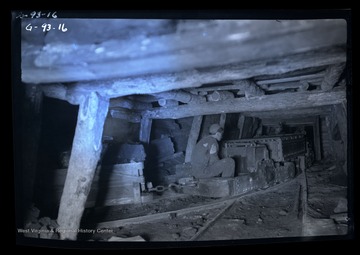 Man sits by controls to loaded mine car.