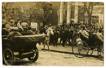 A crowd of people, some in horse-drawn buggies, gathers in anticipation of the WVU Cadet Band.