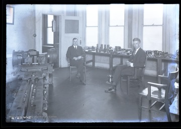 Two men sit next to a machine inside a Goodman Manufacturing Company showroom.