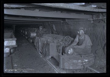 Two men ride on engine hauling loaded coal cars out of mine/