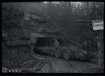 Two men pose on track mounted engine hauling coal car.