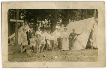 A group of adults and children pose by their tents. A sign on a tree reads "Floater's Rest."