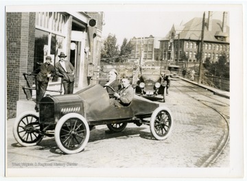 A view looking across the Walnut Street bridge toward the town center. Two men in an early model car are in the foreground.