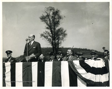 Two American Legion members are on the stage with Louis A. Johnson, who was the national commander of the American Legion in 1932.