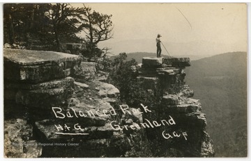 A hiker has climbed to the top of Greenland Gap and is posing on a rock outcrop.