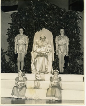 Back of photo reads: "Miss Helen Baker reigned as Queen in a Rhododendron bower as Queen of the May at West Virginia University's annual festival which was a part of Greater West Virginia Week activities. She is a member of Alpha Xi Delta, a candidate for beauty queen, and a member of the university social committee. Bayard Young Photo, Chemistry Building, W. V. U., Morgantown, West Virginia"