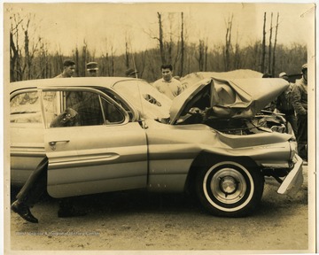 Police officers investigating a recent car wreck in front of onlookers.